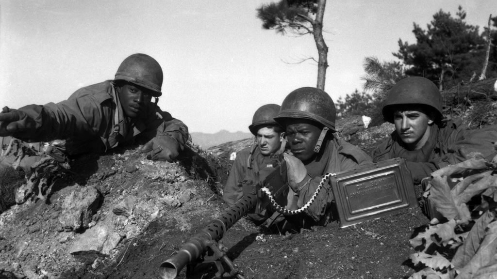 four US soliders, two of which are African American, with large gun in foxhole