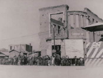 Korean people standing in a line, in front of a deconstructed building