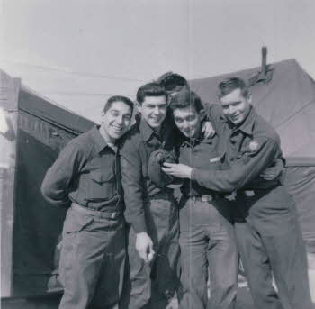 Four soldiers with their arms around each other's shoulders and big smiles.