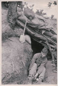 Peter Doyle smoking and tying shoestring in underground tunnel, shovel and grenades are around him