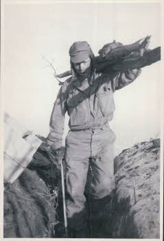 Patrick Anderson, 1st gunner, carrying firewood across ridgeline to MG bunker on forward slope