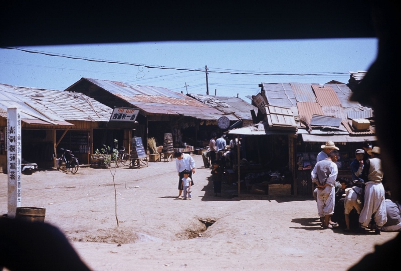 People in an open market in Yong Dong Po, Korea with poor roofing. Taken in 1953.