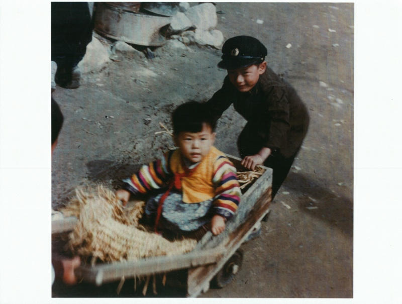 A child pushing a younger child in a wagon in Chuncheon. Taken in 1954.