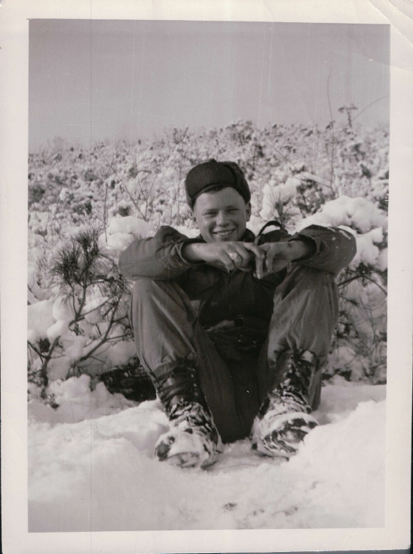 Puls sitting in the snow wearing special Mickey Mouse Boots (called because of its resemblance to Mickey Mouse's boots) which helped keep one's feet warm. Taken in winter of 1953